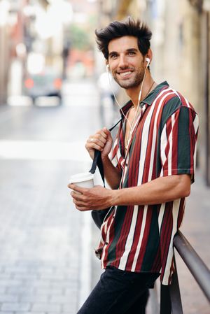Happy male in striped shirt standing in the streets of Granada, Spain with coffee