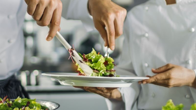 In a Famous Restaurant Cook Prepares Salad and Puts it on a Plate. Working in a Big Modern Kitchen.