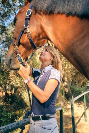 Horsewoman stroking muzzle of horse in paddock
