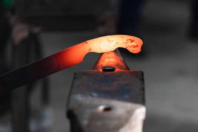 Blacksmiths forging hot metal with hammer in workshop