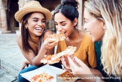 Three cheerful multi-ethnic young women eating Italian pizza at city street 5Qvkg4