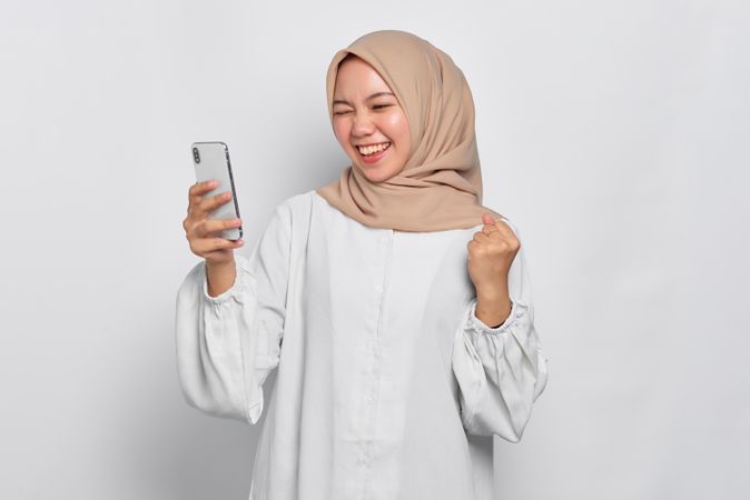 Asian female in headscarf receiving news that she won, through her cell phone
