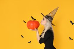 A woman in a wizard's hat kisses a pumpkin, on a yellow background