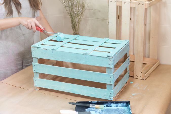 Woman paining wooden box in blue color with roller