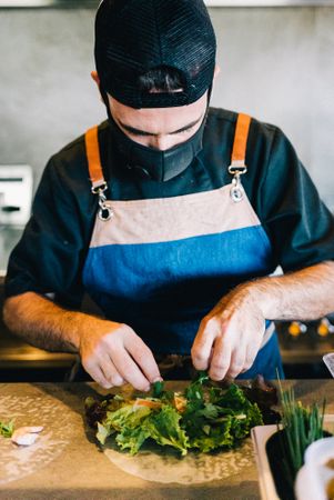 Masked chef head down plating salad dish