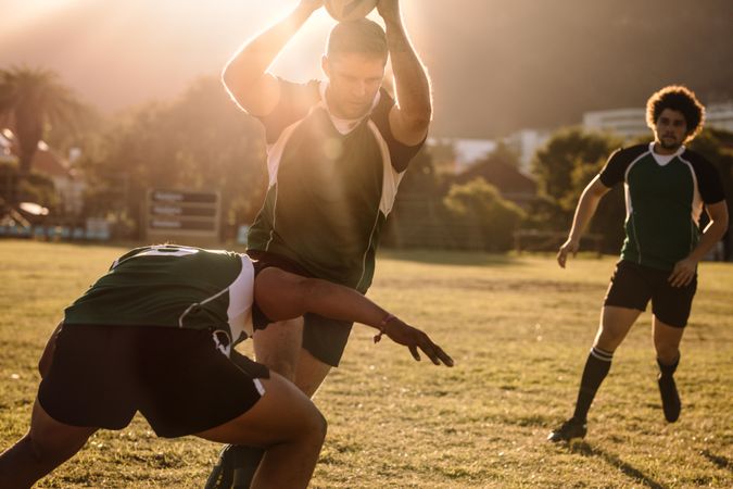 Rugby players running with ball and tackling during game with sun behind