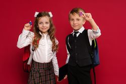Preteens in school uniform carry backpacks on red background