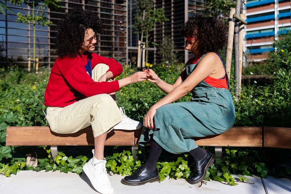 Female friends exchanging flowers on bench outside
