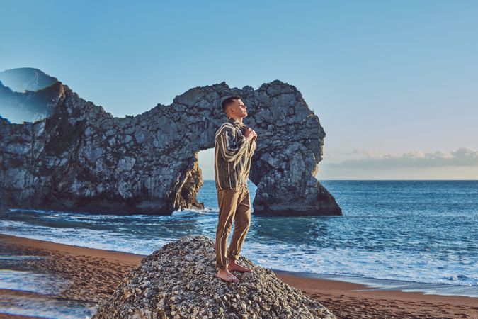 Young man standing on a rock mound on the beach on a clear day