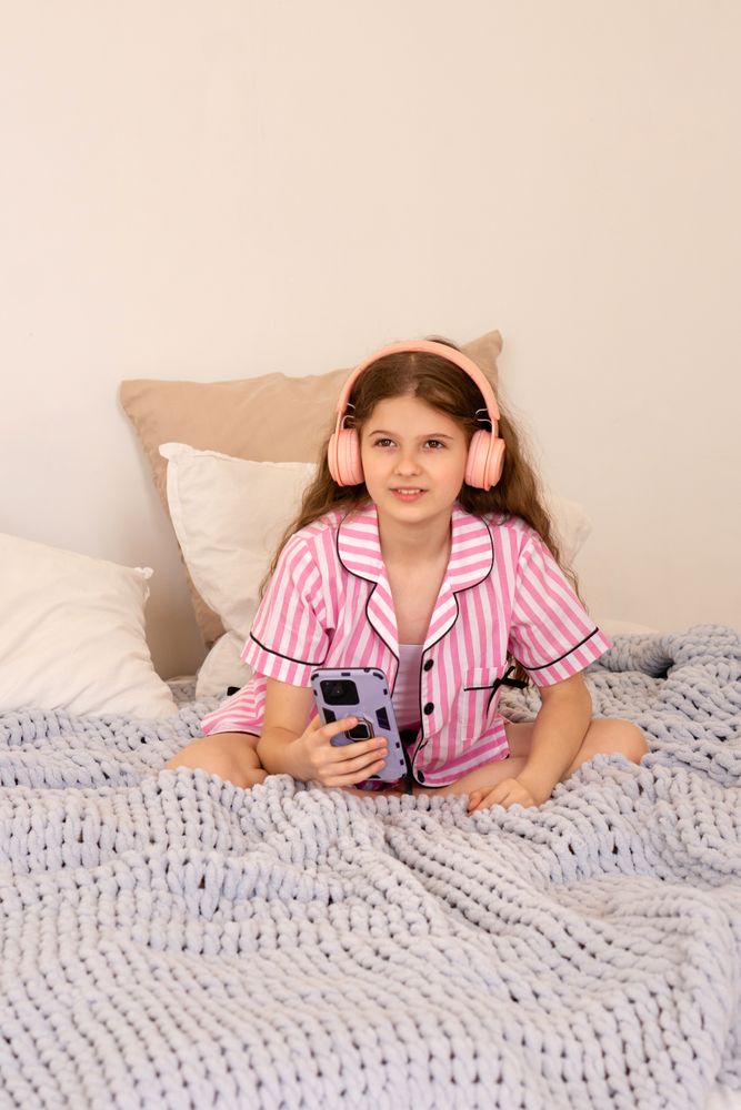 Young girl with headphones using smartphone on bed.