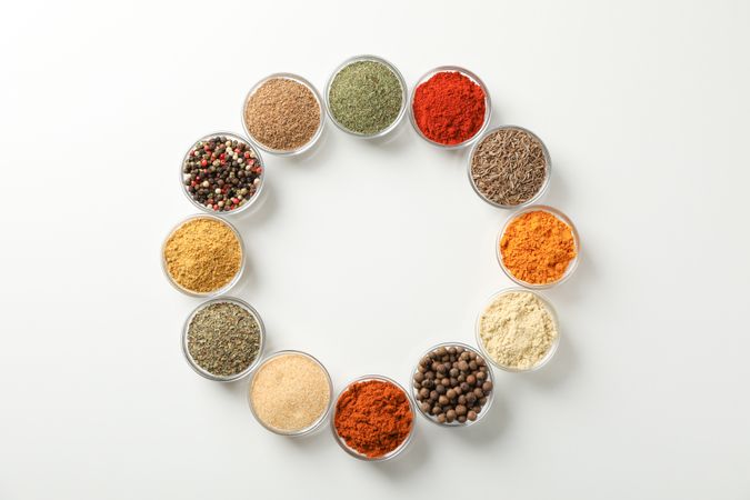 Bowls of colorful spices in circle on plain background with copy space