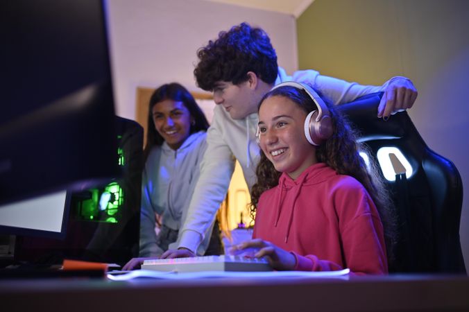 Cheerful diverse friends gathered around gaming PC and enjoying games in room