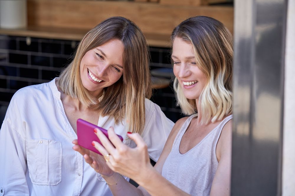 Cheerful women looking through photos on smartphone at restauran