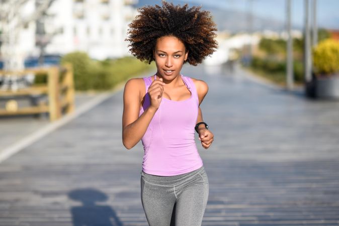 Black woman, with afro hairstyle, running outside in city road