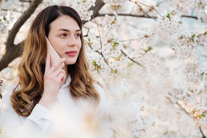 Woman answering phone call near blooming trees