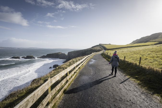 Person walking on country road between sea and field