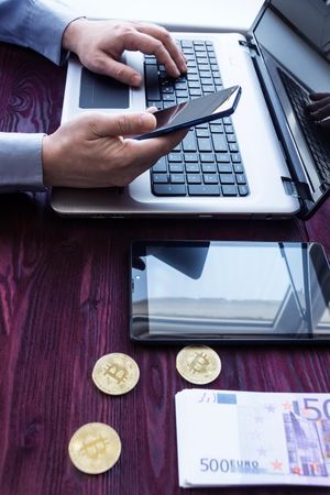 Man using computer beside bitcoins and paper cash