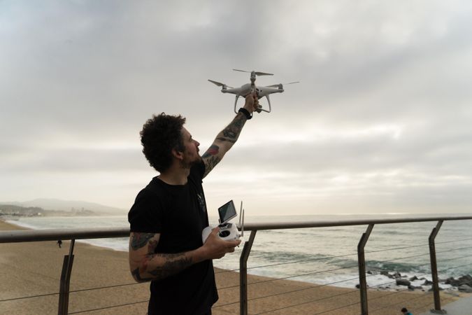 Man holds up drone on wooden boardwalk on beach
