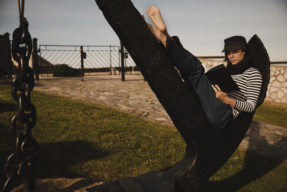 Woman with book sitting on monument near building on shore