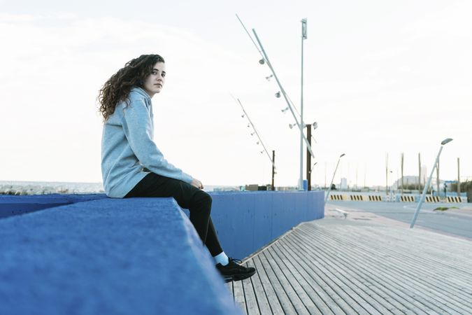 Side view of teenage girl sitting on a blue wall looking camera
