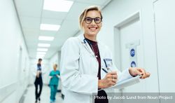 Portrait of happy young female physician standing in corridor with clipboard bDPykb