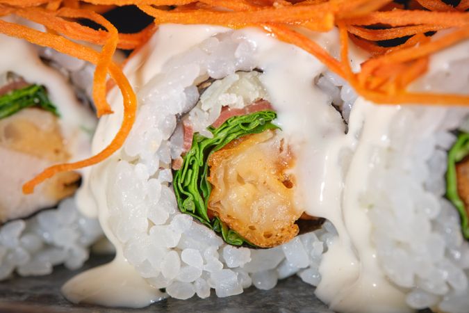 Delicious sushi maki with salmon decorated with shredded carrot and sauce served on plate