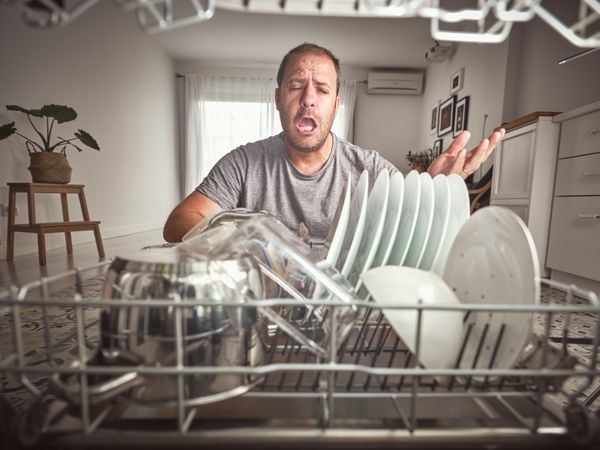 Unhappy man near modern dishwasher