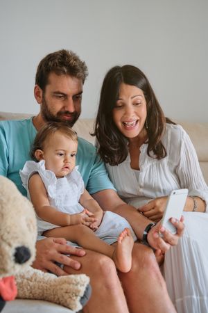 Happy parents with baby using smartphone at home