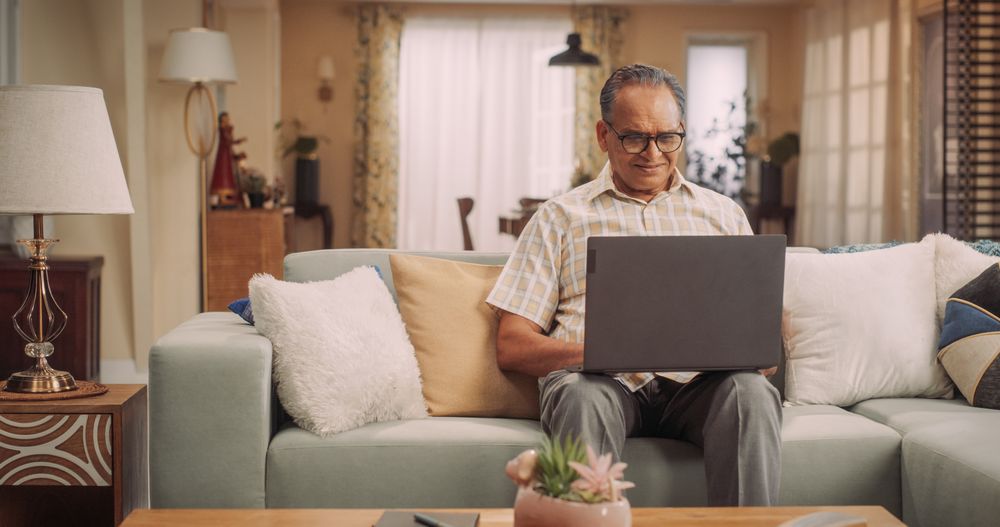 Mature Indian Man Using Laptop at Home: Using Online Forums to Explore Interests, Delving into History, Arts, and Literature.