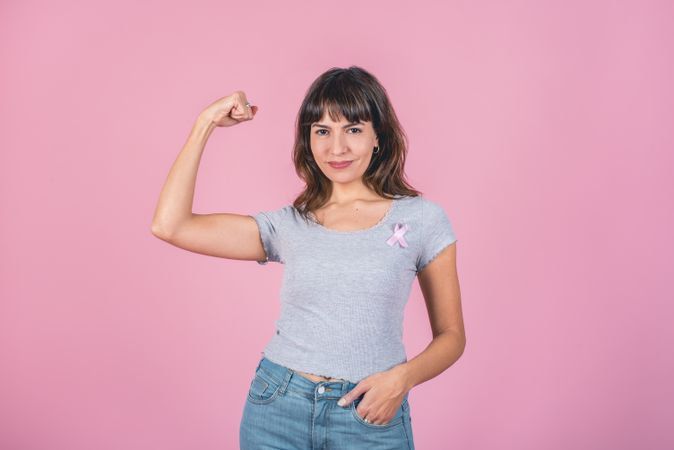 A woman wearing pink breast cancer awareness ribbon while showing arm muscle. Victory over breast cancer.