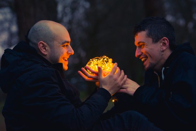 Men holding fairy lights near dog in forest at night