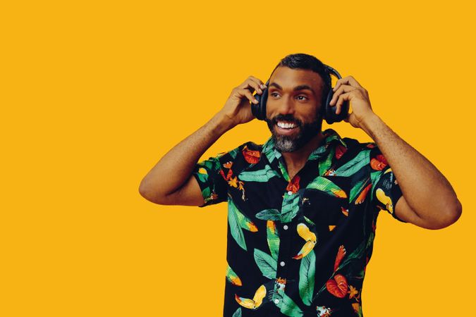 Smiling Black male in bold patterned shirt putting on headphones in yellow room