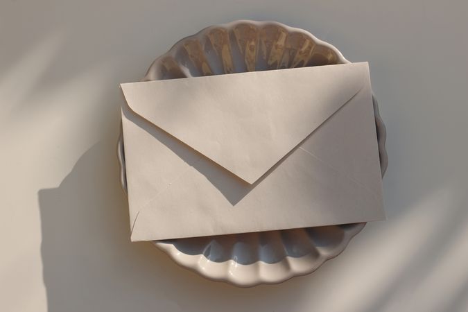 Closed beige envelope on plate with shadows