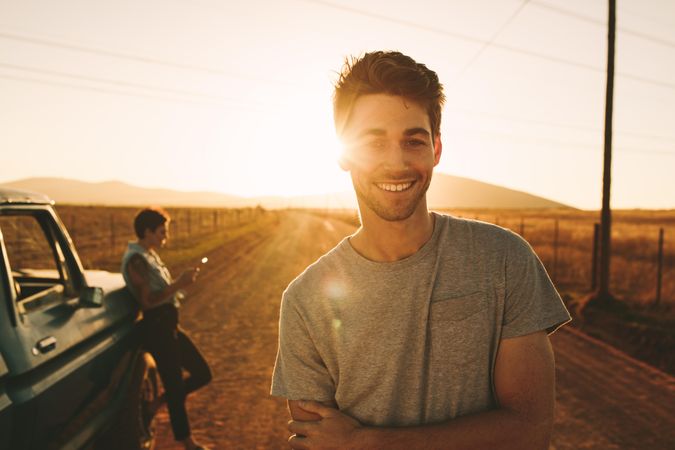 Young man smiling looking at camera while girlfriend is leaning on classic truck in background