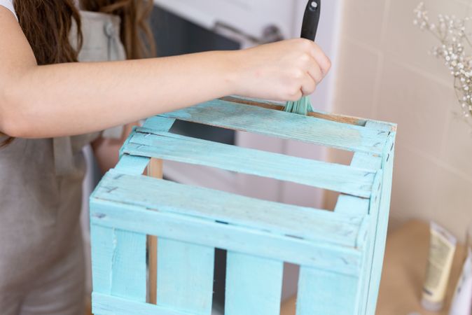 Woman paining wooden box in blue color with brush