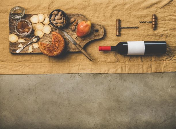 Cheese plate with bottle of red wine, cork screws, on light brown linen, over concrete, copy space