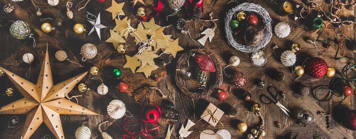 Holiday decorations of stars, baubles, scissors and ribbon strewn on wooden table, wide composition