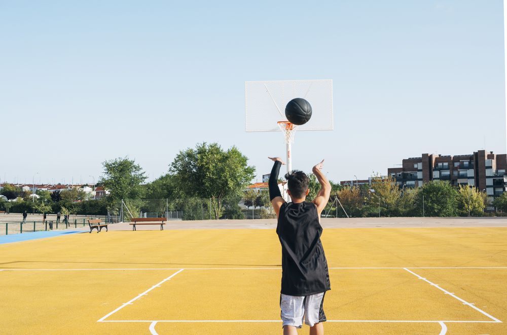 Young man playing on yellow basketball court outdoor.