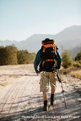 Rear view of man with backpack walking over a mountain trail 0vGyd5