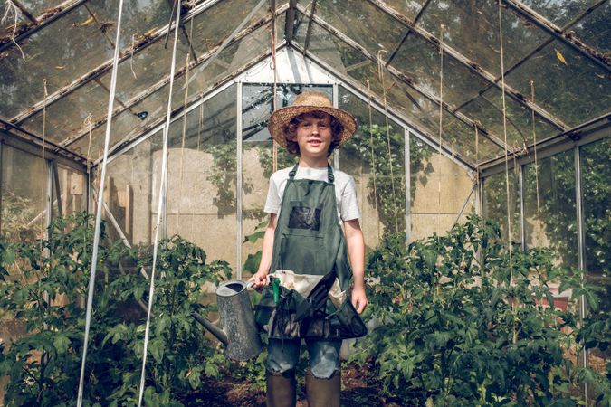 Preteen boy gardener with watering can in glasshouse