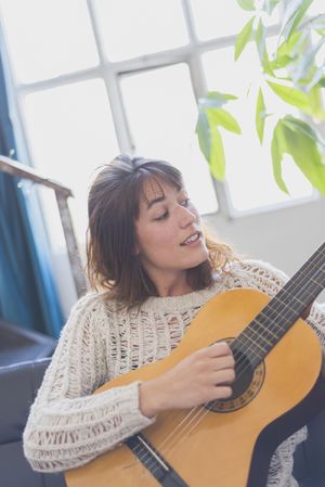 Female singing along while strumming guitar in living room of bright loft