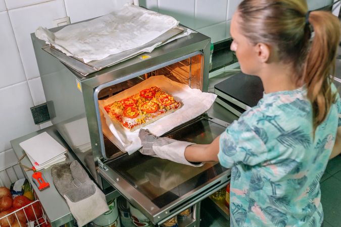 Unrecognizable professional cook taking pizza out of oven in restaurant kitchen