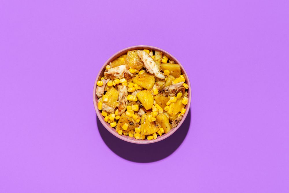 Pineapple chicken salad bowl, above view on a purple background