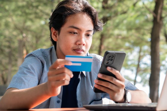 Happy Asian Young businessman hold blue creditcard and phone purchasing online shopping in outdoor cafe.