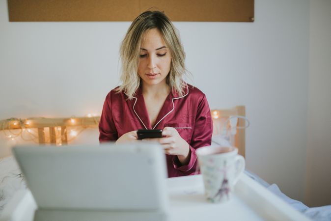 Woman sitting in bed with tablet and looking on smartphone