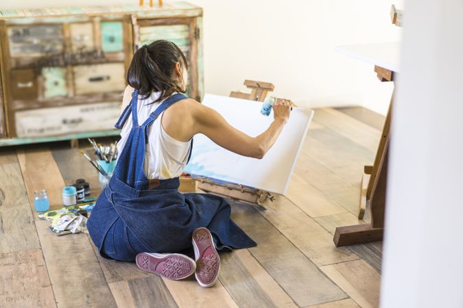Woman artist painting on a canvas a blue abstract painting. Creative ywoman working on the floor in her art studio.