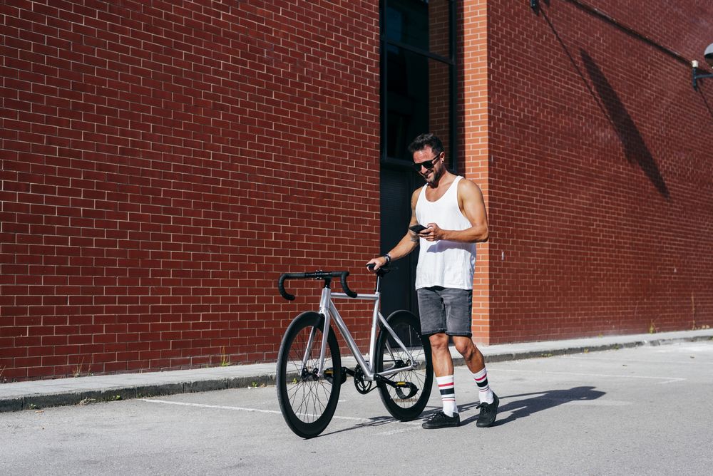 Sportive man with bicycle using phone