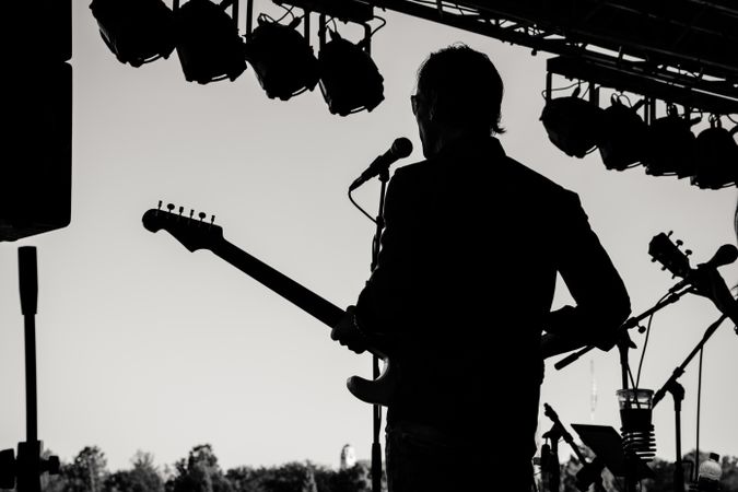 Back view of man singing and playing guitar on stage in grayscale