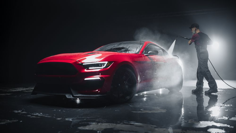 Adult Car Detailer in Uniform Washing a Red Sportscar with a High Pressure Cleaner.