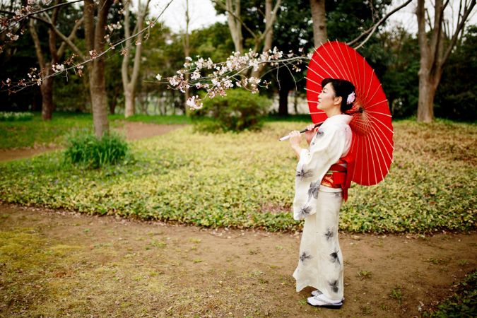 Japanese woman in kimono holding red oil-paper umbrella standing in a garden